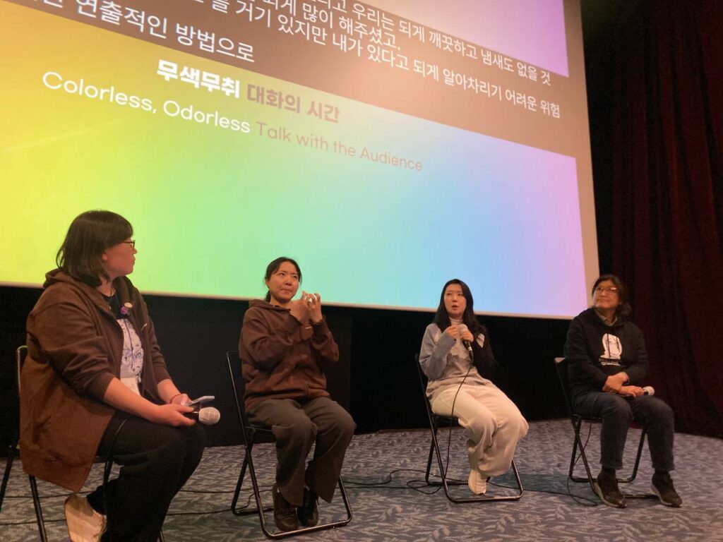 극장 공간 앞 무대 위에 네 명의 사람이 앉아 마이크를 잡고 이야기를 하고 있다. 무대 뒤 스크린에는 무지개색 배경 위 검정색 박스에 실시간 문자통역 글자가 흰색으로 비치고 있다.
: 30회 인천인권영화제 <무색무취>대화의 시간 풍경