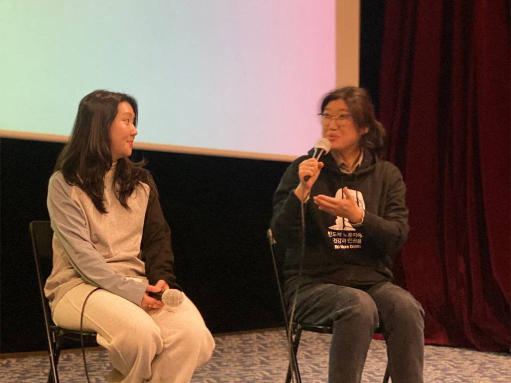 극장 공간 앞 무대 위에 두 명의 사람이 앉아 마이크를 잡고 이야기를 하고 있다. 무대 뒤 스크린에는 무지개색 배경 위 검정색 박스에 실시간 문자통역 글자가 흰색으로 비치고 있다.
: 30회 인천인권영화제 <무색무취>대화의 시간 풍경